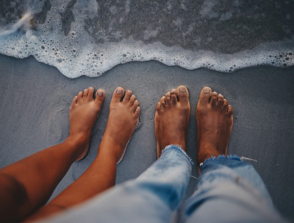 Couple feet, beach sand and water at ocean waves, nature and summer travel for vacation, honeymoon